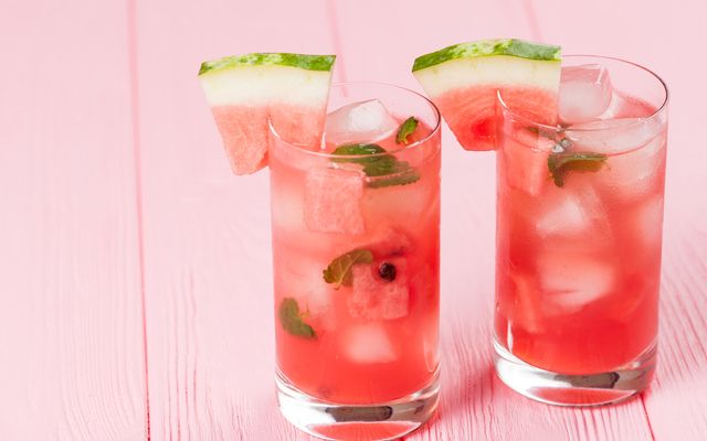 Watermelon lemonade with ice and mint leaves. Homemade lemonade of ripe berry with red and green ripes. Glass of cold watermelon tea. Refreshing summer drink. Cocktail on a wooden background
