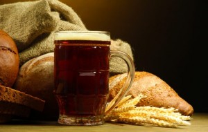 tankard of kvass and rye breads with ears, on wooden table on brown background