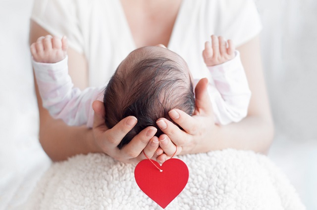 Проблеми із серцем у дитини: як виявити Mother holding head of her newborn baby in hands. Happy family concept. Maternal love and parental love. Red heart hanging from the arms.